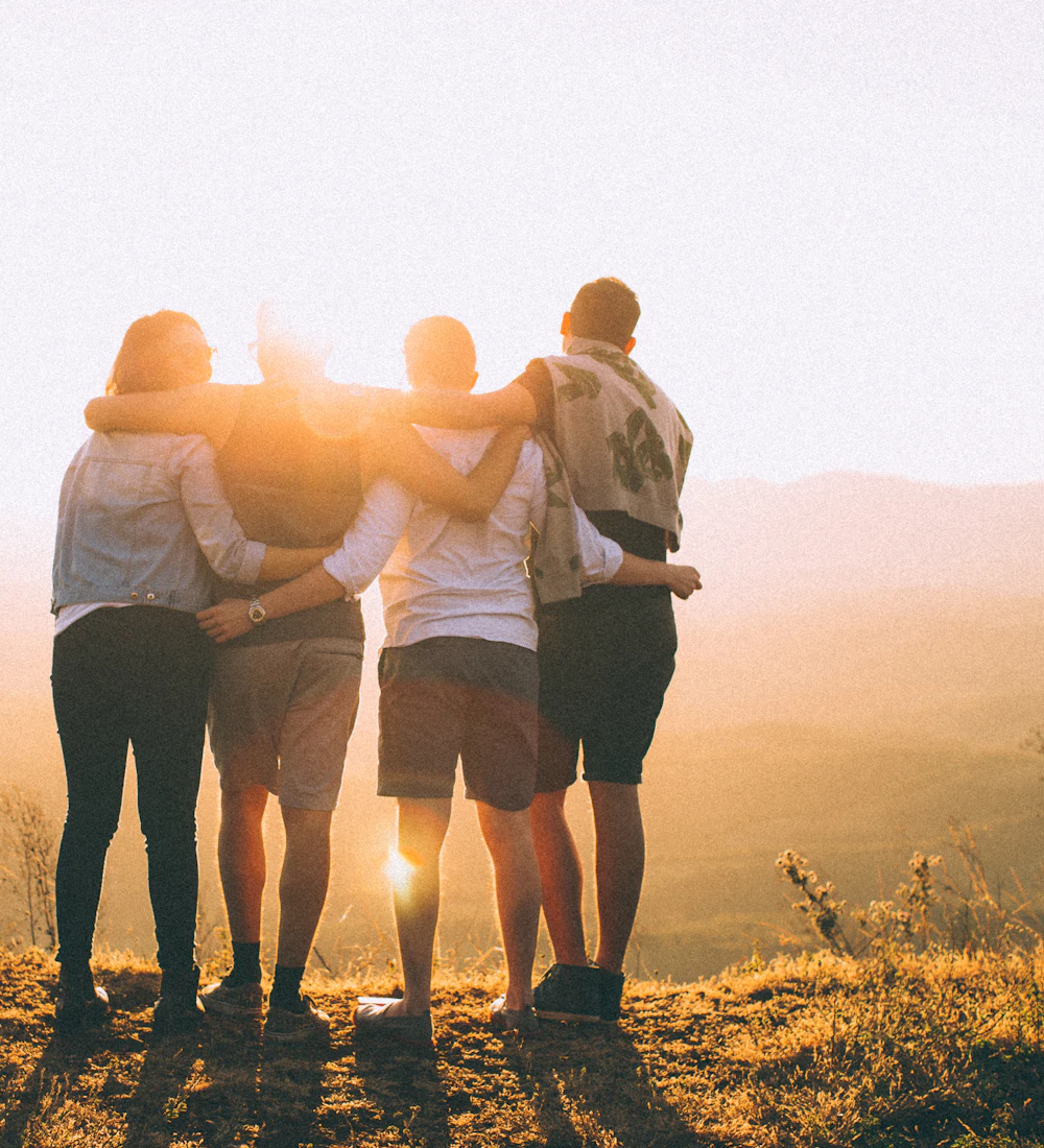 Friends with their arms around each other, facing the sunrise